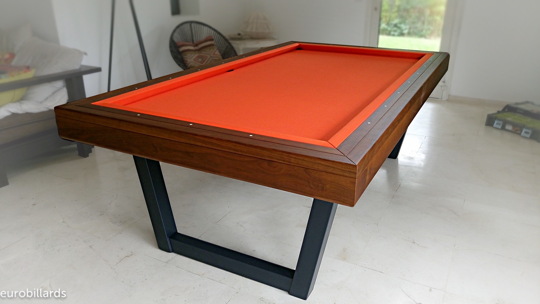 Ce client a choisi Eurobilards comme marque de billard français avec ce modèle HARMONY-V en bois massif de noyer mis en exergue par le orange du tapis de jeu qui illumine la pièce. Posé sur son piétement métallique noir en acier inoxydable, cet achat de billard est doublement malin, grâce à l'acquisition de notre système XB qui transforme très rapidement les bandes de billard français en billard américain aux normes des compétitions.